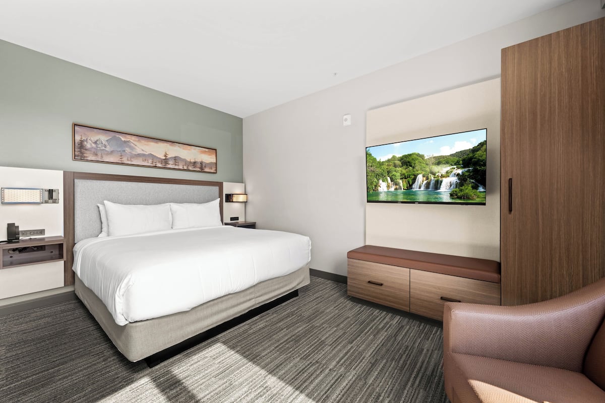 Ein modernes Hotelzimmer mit Bett, Fernseher, Schreibtisch und Kleiderschrank.