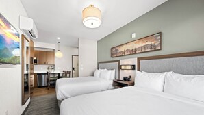 A hotel room with two beds, a desk, a chair, a small kitchenette, and a painting on the wall. - The Kulshan Hotel (Sedro-Woolley)