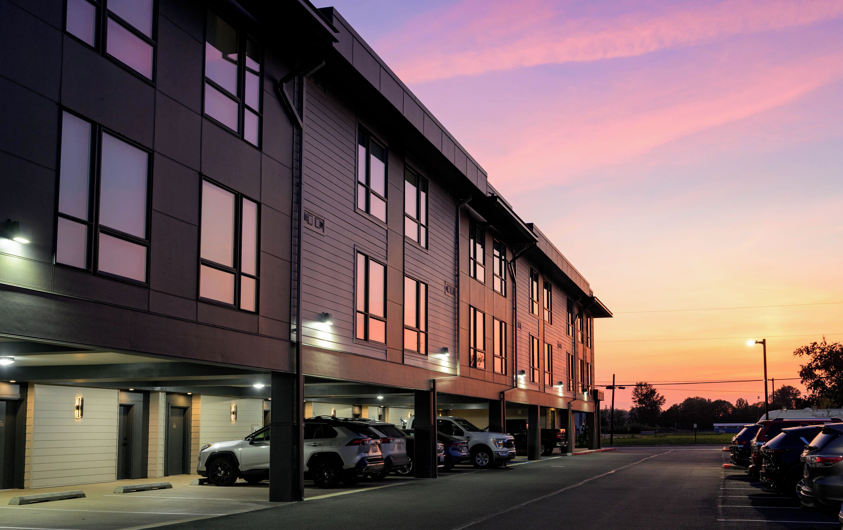 A modern building with multiple parking spaces and a row of parked cars.