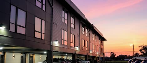 A modern building with multiple parking spaces and a row of parked cars.