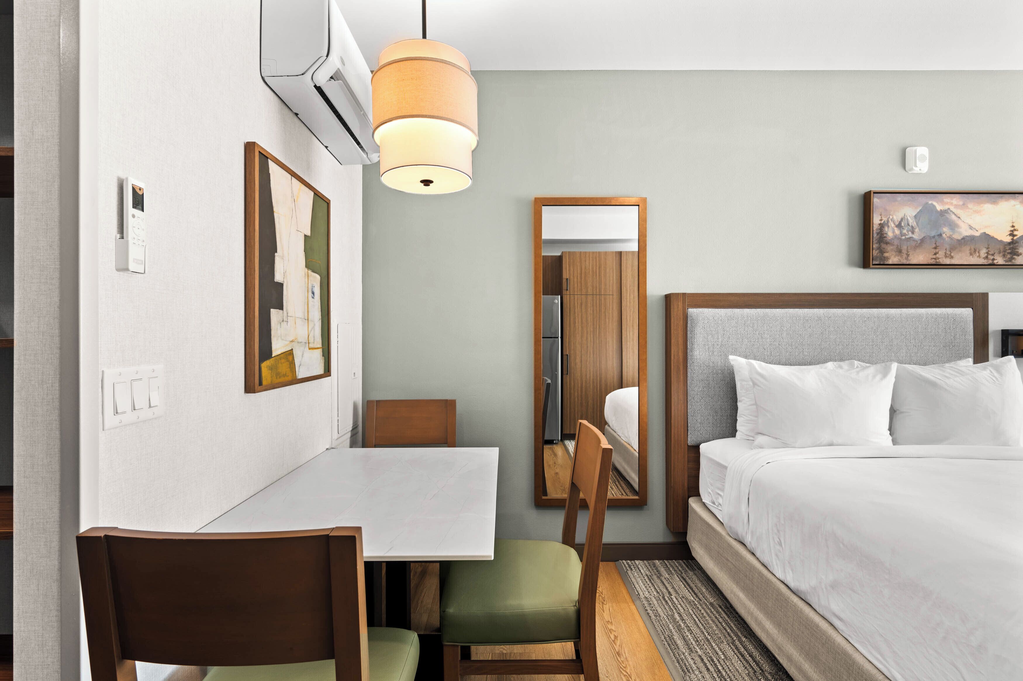 A hotel room with a bed, a desk, a chair, a painting, and a mirror.