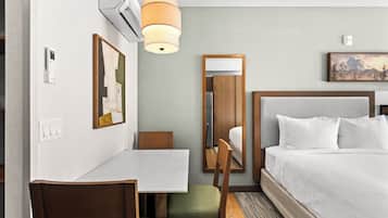 Una habitación de hotel con cama, escritorio, silla, un cuadro y un espejo.