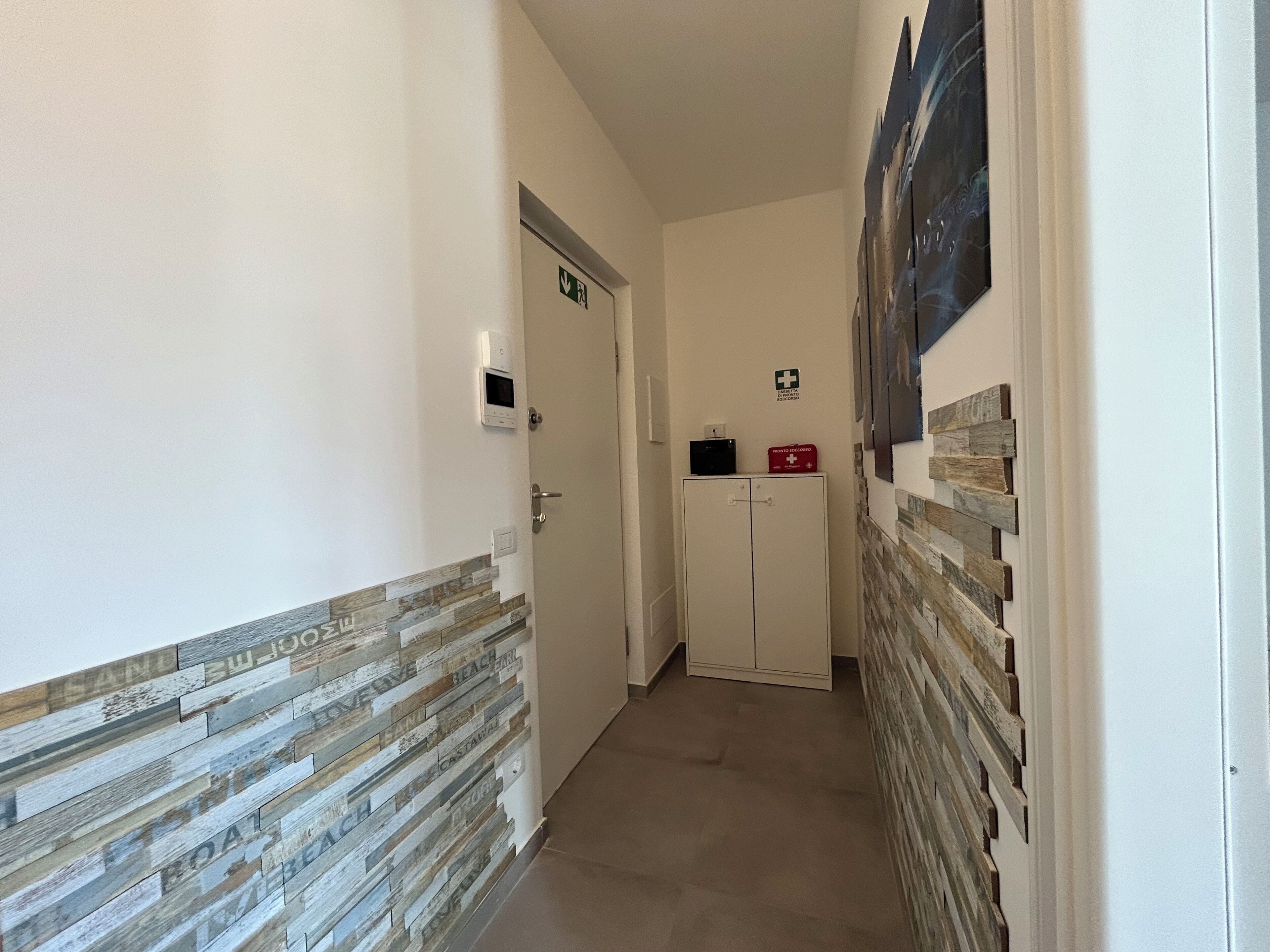 A hallway with a white door, a medical emergency sign, a digital clock, and a red emergency box.