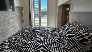 Ein Schlafzimmer mit Bett, Kleiderschrank, Fernseher und Blick ins Freie.