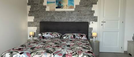 A bedroom with a stone wall, a bed with floral bedding, two bedside lamps, and a door.
