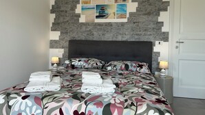 Ein Schlafzimmer mit einem Kopfende aus Stein, einer blumigen Tagesdecke und ordentlich gefalteten Handtüchern.