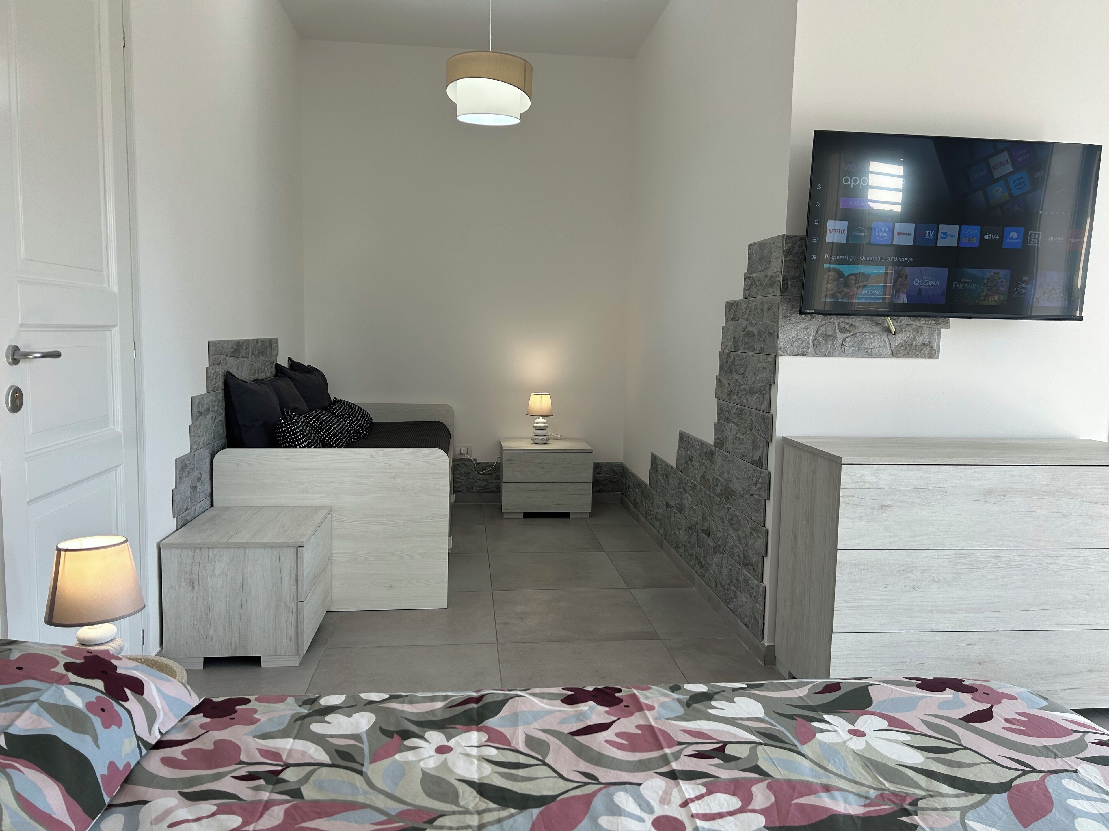 A bedroom with a bed, bedside table, lamp, and a TV mounted on the wall.
