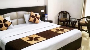 Un lit bien fait, recouvert d’une couvre-lit marron et blanche, avec une tête de lit et deux coussins décoratifs. On y trouve une petite table avec des chaises et un tableau d’affichage en liège accroché au mur.