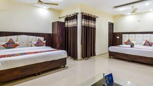 Une chambre d’hôtel avec deux lits, un ventilateur de plafond, une fenêtre avec des rideaux et une petite table sur laquelle est posé un panneau.