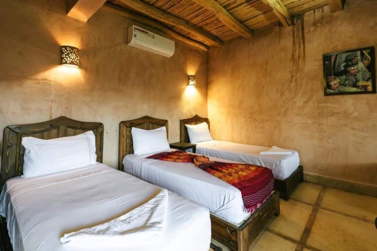 A room with three beds, wooden headboards, and two wall-mounted lights.