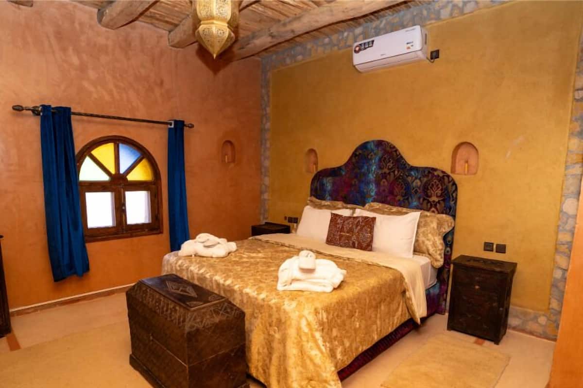 A bedroom with a large bed, a nightstand, a chest of drawers, and a window with blue curtains.
