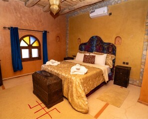 A bedroom with a large bed, a nightstand, a chest of drawers, and a window with blue curtains. - Palais d'Ouzoud (Ait Taguella)
