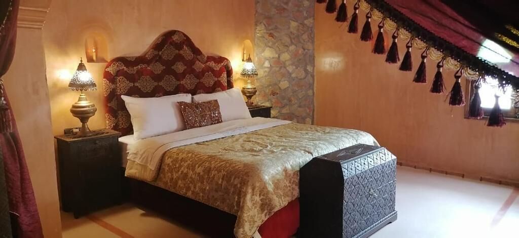 Una cama con una colcha estampada, dos lámparas de noche y un cabecero decorativo.