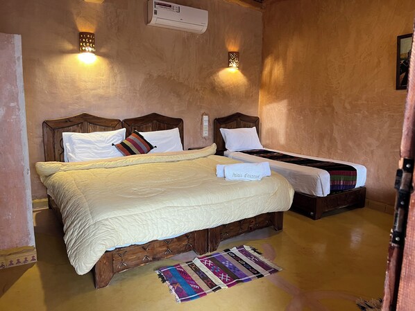 A double bed with a white duvet and a colorful striped pillow, a smaller single bed with a white duvet, and a patterned rug on the floor. - Palais d'Ouzoud (Ait Taguella)