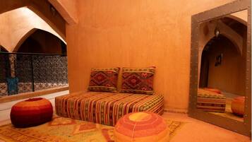 A bedroom with a bed, two pillows, a red ottoman, and a patterned rug.