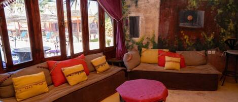 A cozy seating area with cushioned benches and a small table, large windows with curtains, and a mural on the wall.