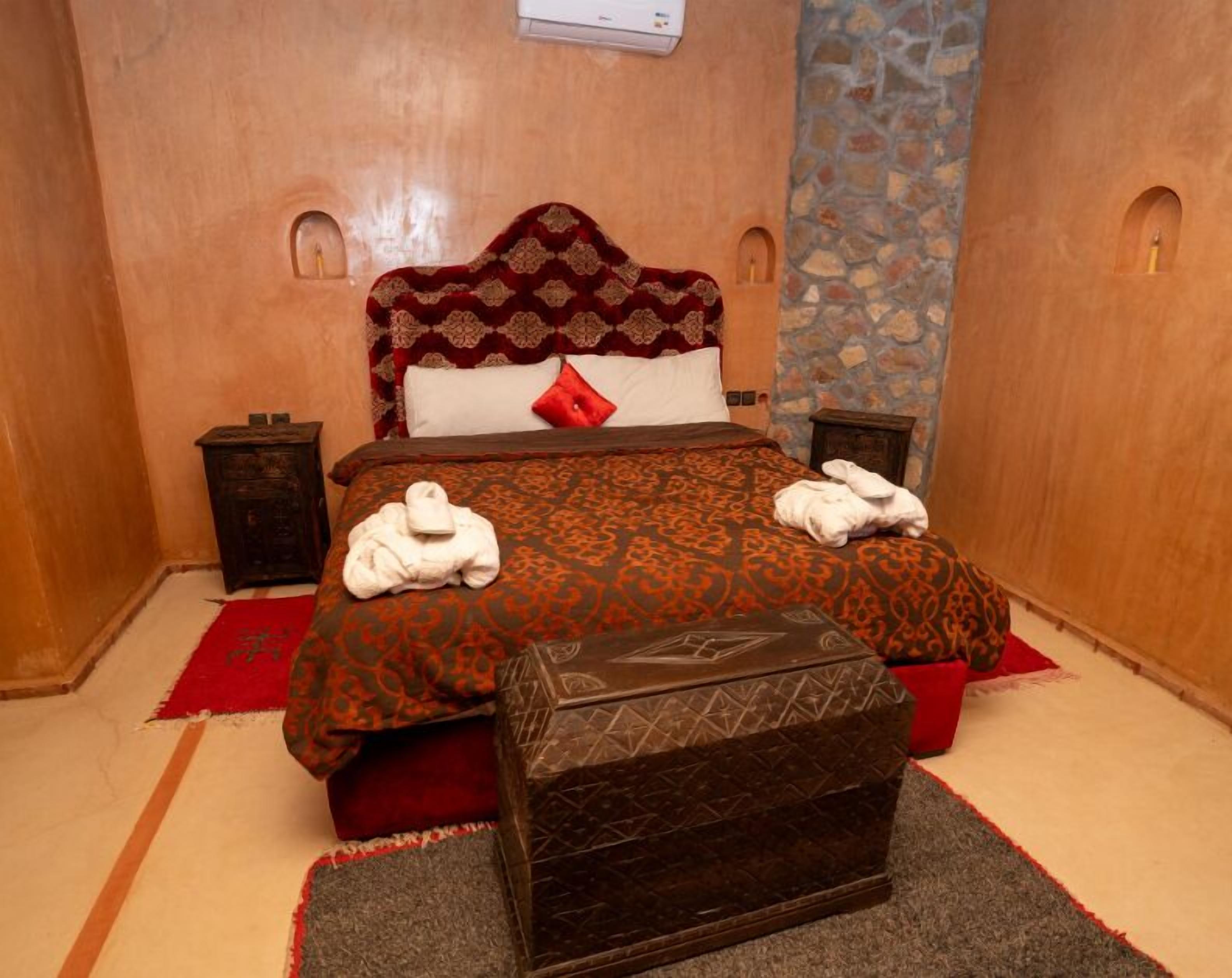 A neatly arranged hotel room with a patterned bedspread, a headboard, two bedside tables with lamps, and a small chest of drawers.