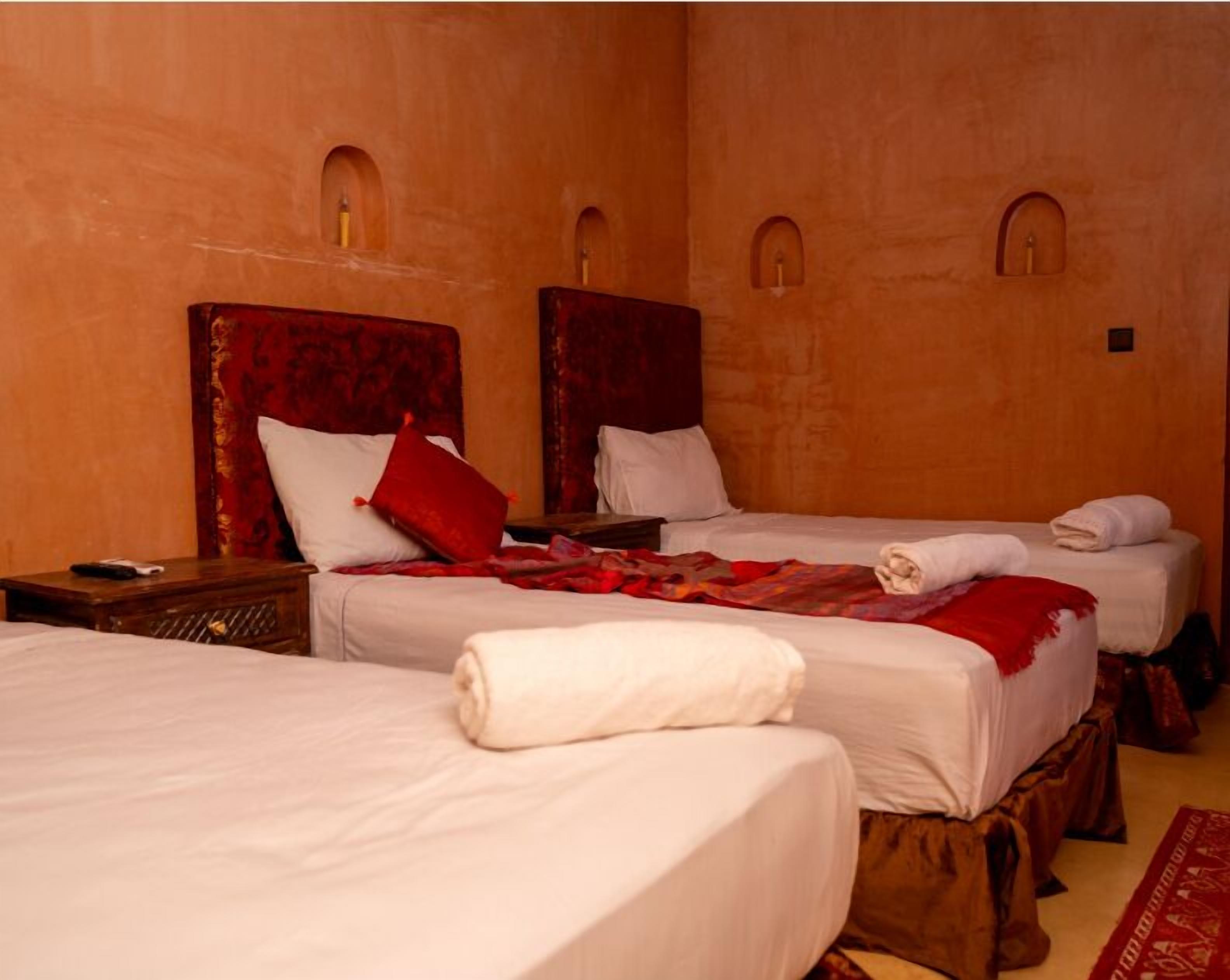 A hotel room with three beds, each with a red headboard, white bedding, and a red throw blanket.