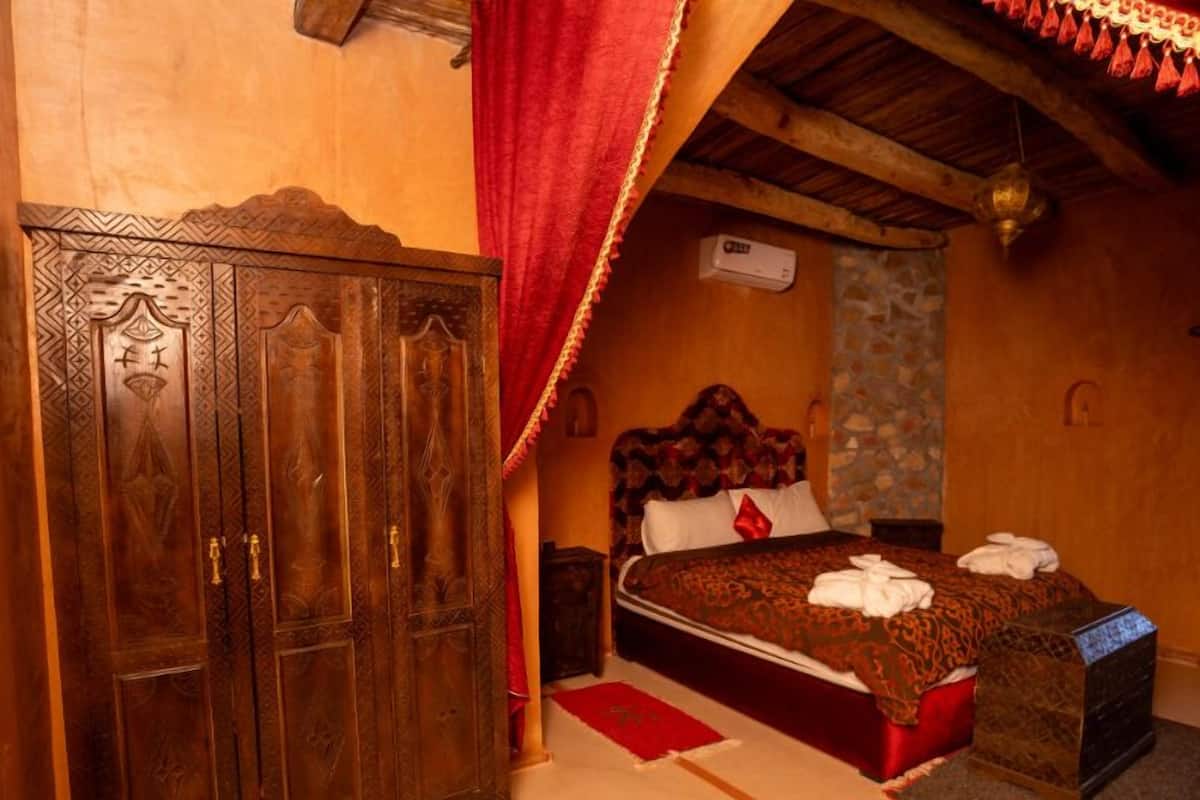 A traditional room with a wooden wardrobe, a bed with a patterned bedspread, and a red curtain.