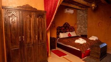 A traditional room with a wooden wardrobe, a bed with a patterned bedspread, and a red curtain.