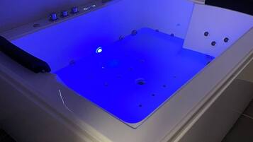 A modern, rectangular hot tub with a blue light feature, set in a room with tiled flooring and a neutral color scheme.