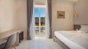 A hotel room with a bed, a desk, and a balcony with a view of a building and flowers.