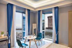 A modern hotel room with a balcony, a dining table with chairs, a bed, and a view of a historic building.