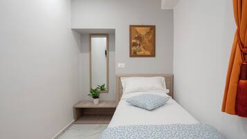 A bedroom with a bed, a potted plant, a painting, and a door.