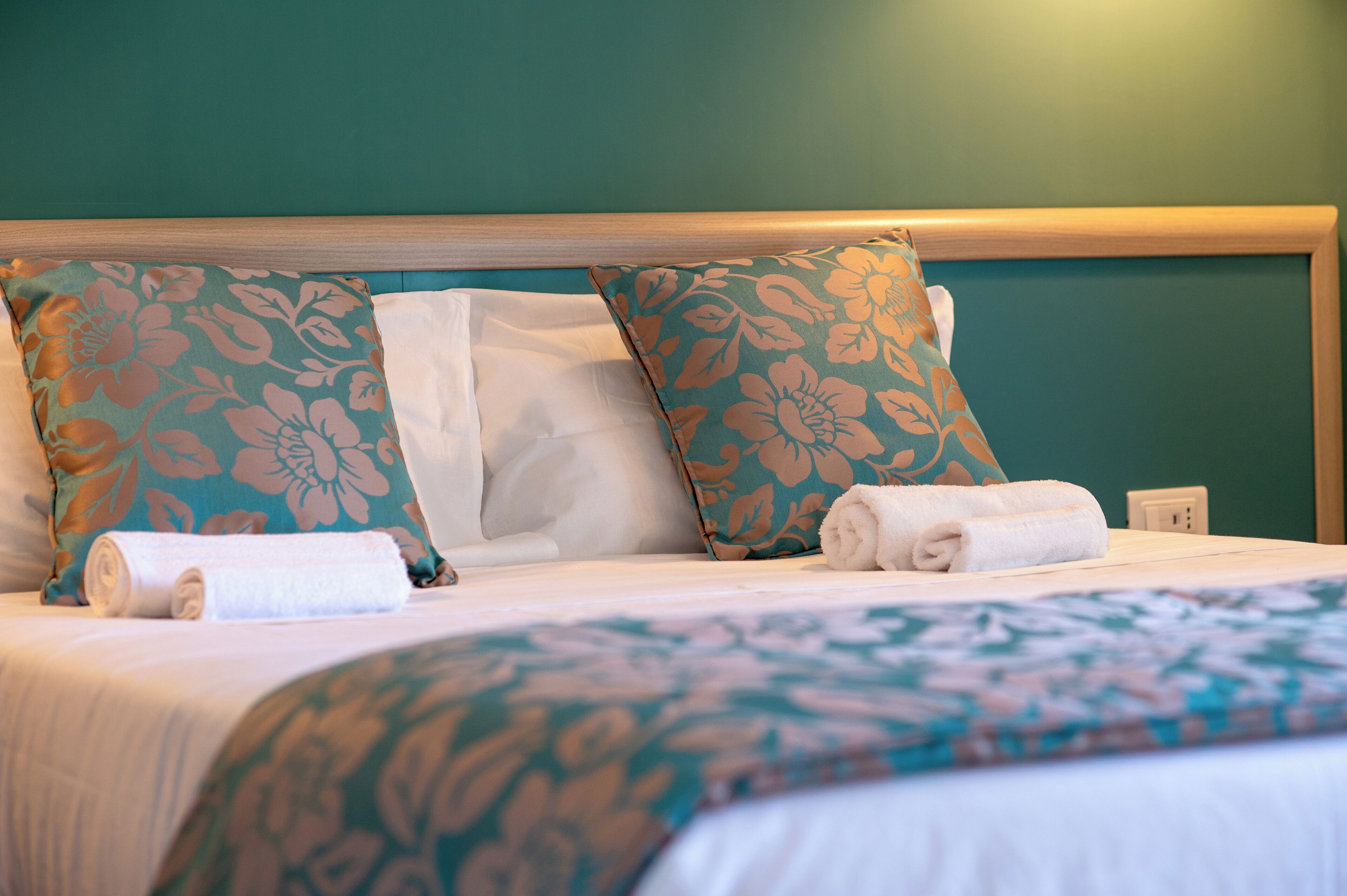 A neatly made bed with floral-patterned pillows and a rolled white towel.