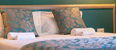 A neatly made bed with floral-patterned pillows and a rolled white towel.