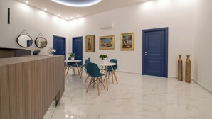 Un área de recepción moderna con un mostrador de madera, sillas color turquesa y piso de mármol blanco.