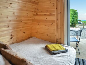 Une chambre confortable dans un chalet, avec des murs en bois, un lit recouvert d’une couverture blanche, une serviette jaune et une petite table avec une chaise à l’extérieur.