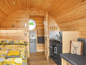 Un interior pequeño y de madera con una cama, una kitchenette y un espacio para sentarse.