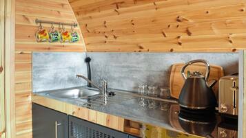A kitchen with wooden walls, a stainless steel sink, a kettle, and a toaster.