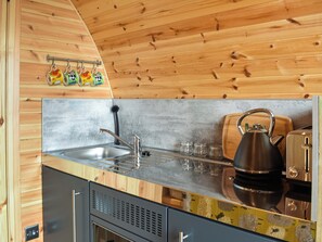 Una cocina con paredes de madera, un lavamanos de acero inoxidable, una tetera y un tostador.