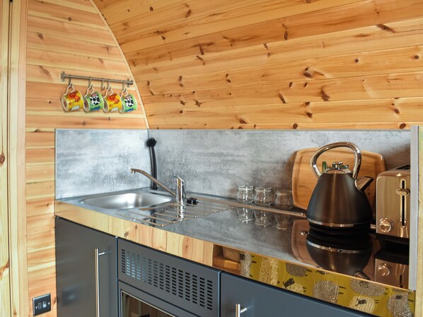 Une cuisine avec des murs en bois, un évier en acier inoxydable, une bouilloire et un grille-pain.