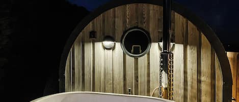 Een jacuzzi voor een houten gebogen constructie met een schoorsteen waar rook uit komt.