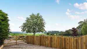A wooden fence with a gate, gravel ground, and a tree in a rural setting.