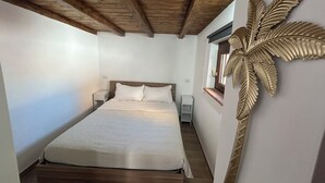A bedroom with a wooden ceiling, a bed with white bedding, a nightstand, a small table, and a decorative palm leaf on the wall. - Appartamento per Vacanze-Casa Sole (Fiumicino)