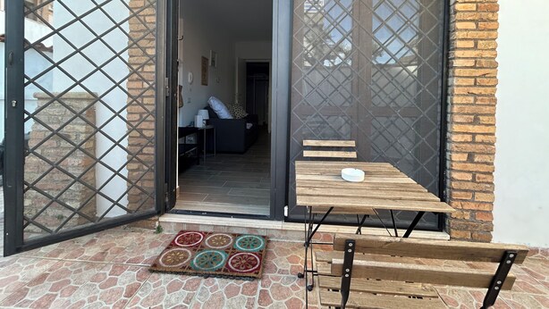 A patio area with a wooden table and benches, a door leading to an interior space, and a patterned rug on the floor. - Appartamento per Vacanze-Casa Sole (Fiumicino)
