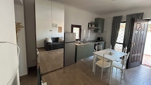 A compact kitchen with a refrigerator, stove, and dining area with chairs and a table. - Appartamento per Vacanze-Casa Sole (Fiumicino)