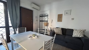 A dining area with a white table and chairs, a dark sofa with polka dot pillows, and a door with a curtain. - Appartamento per Vacanze-Casa Sole (Fiumicino)