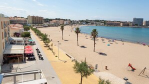 Ein Strand mit einer Reihe von Palmen, Sonnenschirmen und Gebäuden mit Balkonen.