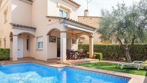 A swimming pool with a tiled edge, a covered patio with outdoor furniture, and a building with a tiled roof and arches. - Casa Hermosa (L'Escala)