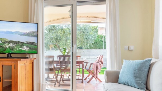 A living room with a television, a sofa, and a dining area with chairs and a table. - Casa Hermosa (L'Escala)