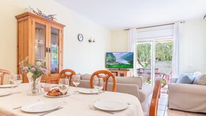 A dining area with a table set for two, a wooden cabinet, a television, and a sofa. - Casa Hermosa (L'Escala)