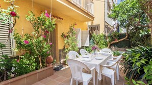 A patio with a table set for dining, surrounded by plants and a yellow building.
