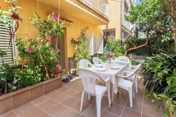 A patio with a table set for dining, surrounded by plants and a yellow building.