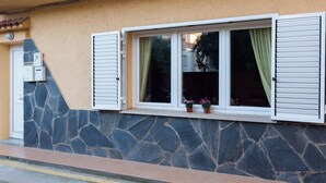 A building with a stone facade, a window with white shutters, and a small balcony with potted plants.