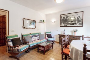 A living room with a sofa, chairs, a coffee table, a dining table, and a framed photograph on the wall.
